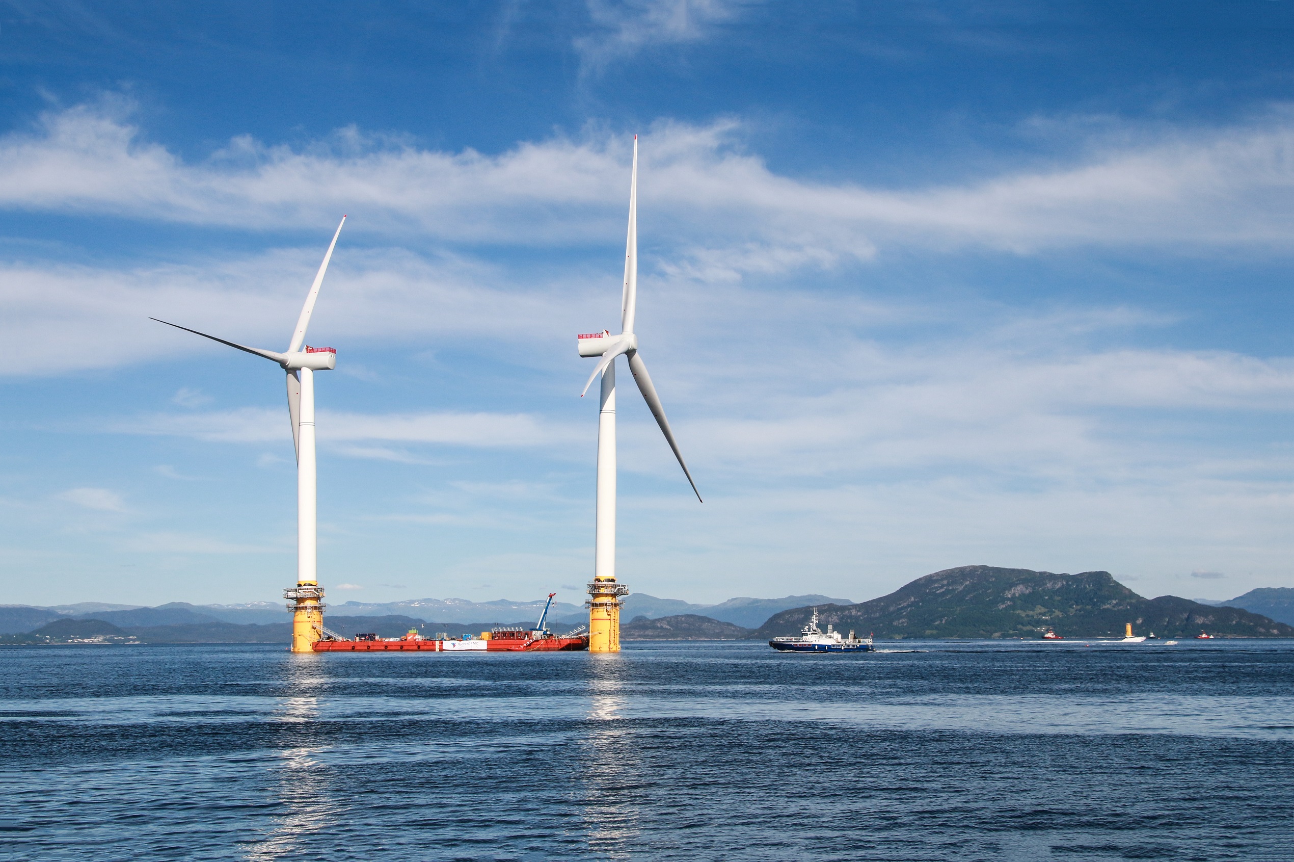 Two offshore wind turbines, mountains in background