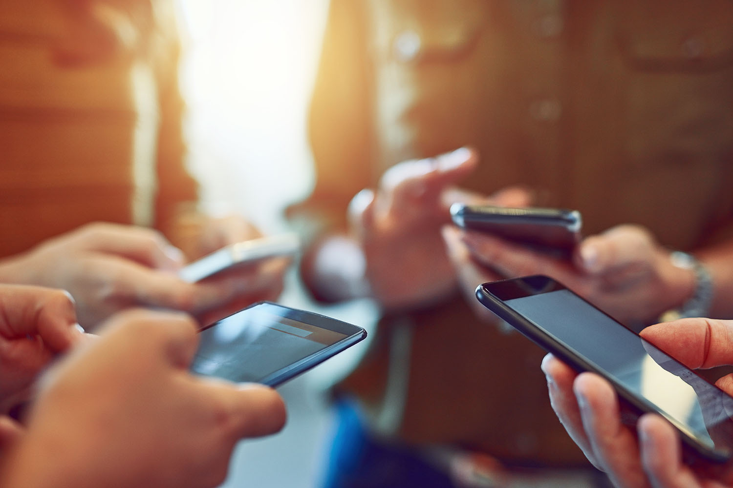 Four people in a circle, close up view of them holding and typing on their smartphones