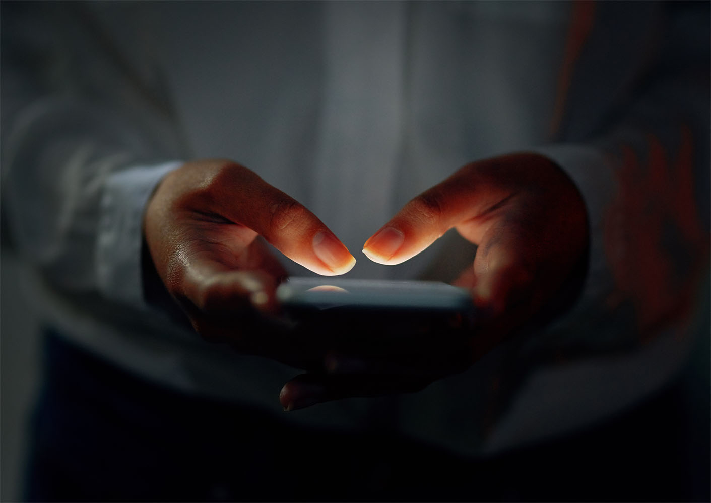 Person holding a smartphone, dark background, phone lit up