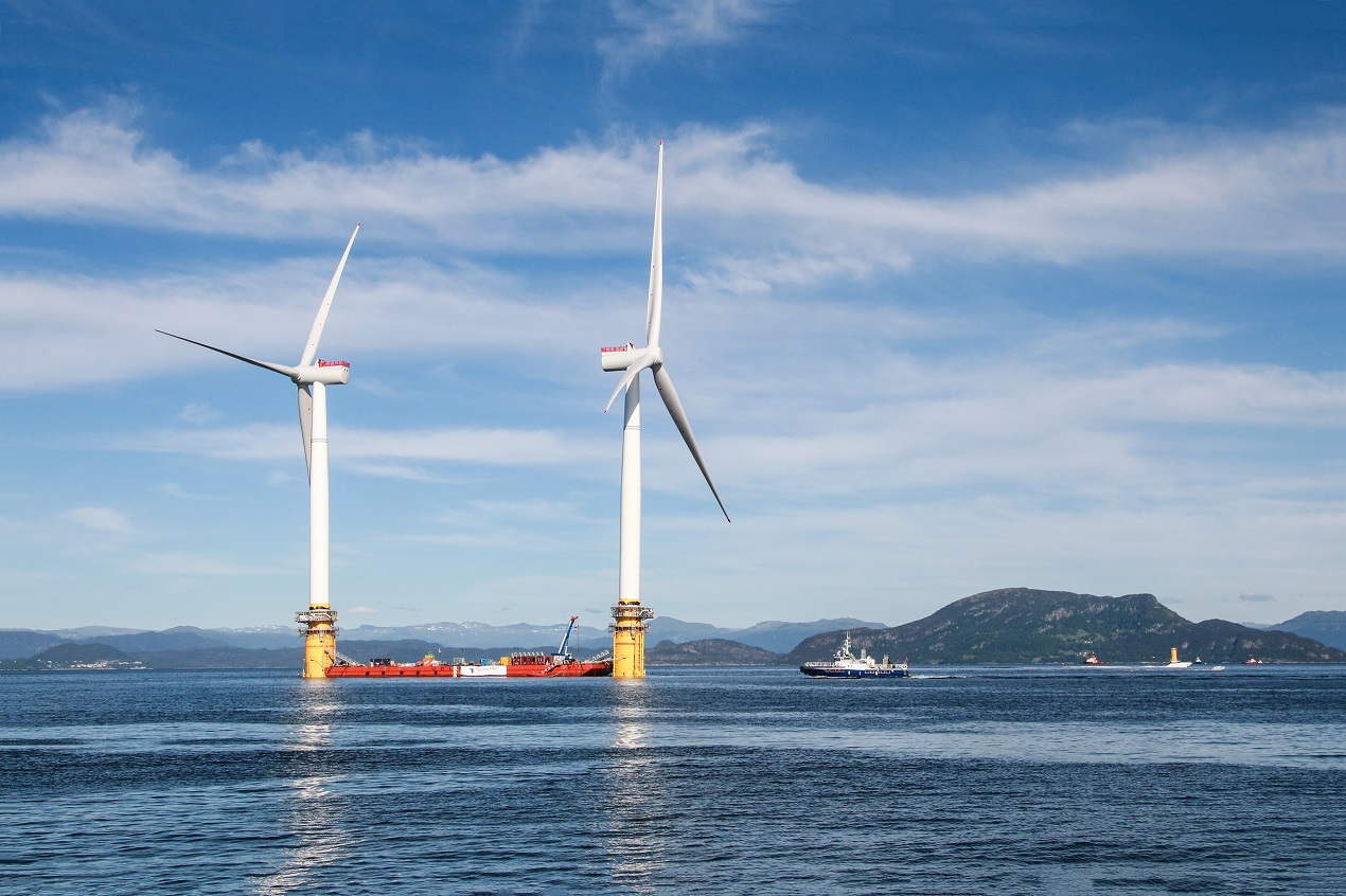 Two offshore wind turbines, mountains in background