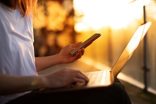 Person working with a laptop on their lap and phone in their hands