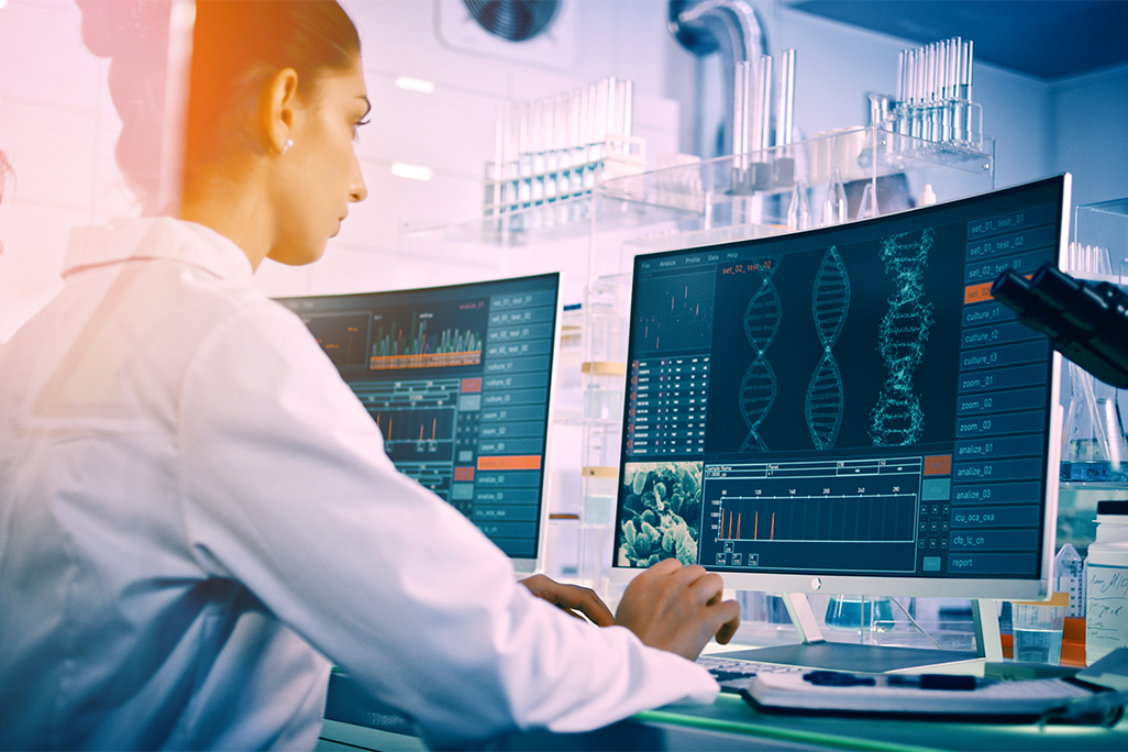 Person in white lab coat looking at medical data on computer screen