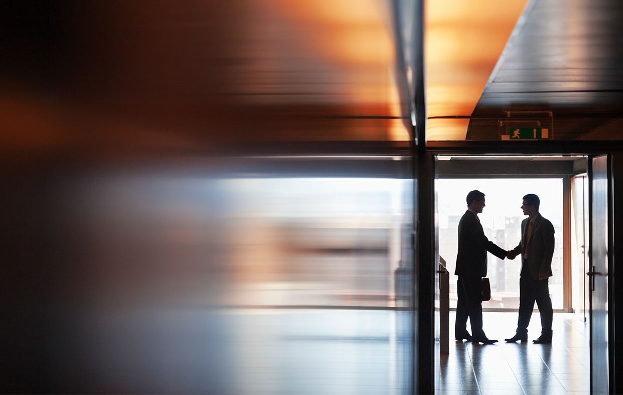 Two men shaking hands at the end of a corridor 